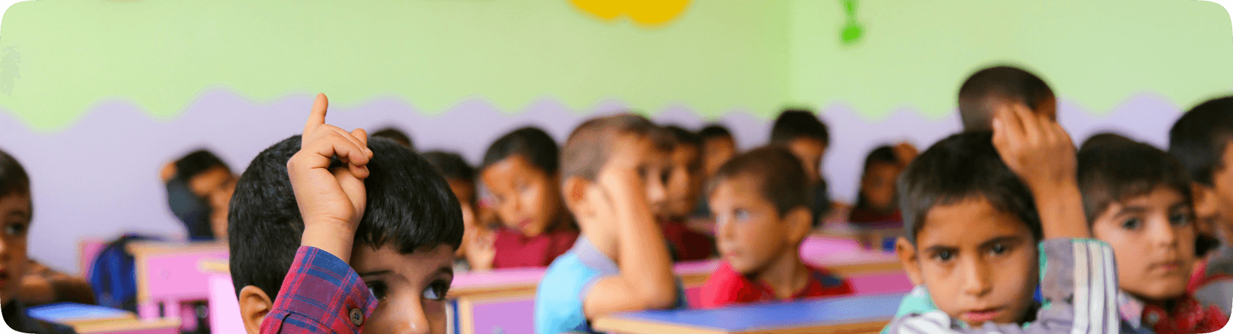 Children sitting in a classroom with hands raised, representing Pararthya SDECS education initiatives