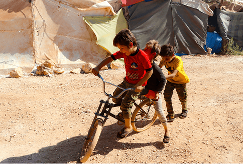 Children riding bicycles on a dusty road in a Pararthya SDECS community