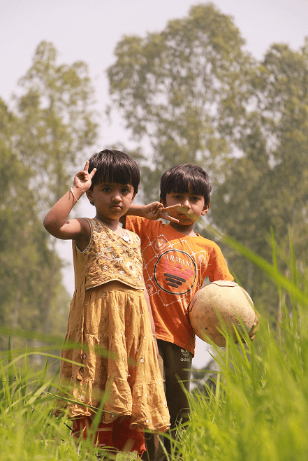 Children standing in a lush green field — rural communities served by Pararthya SDECS