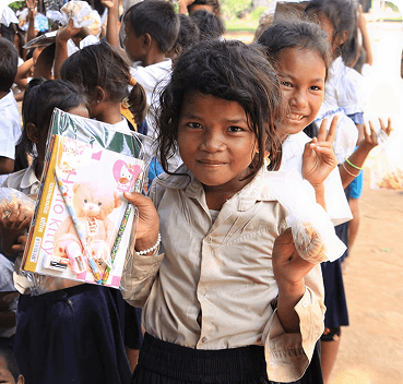 A schoolgirl holding books and smiling at a Pararthya education camp